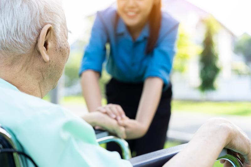 carer holding had with elderly person in wheelchair