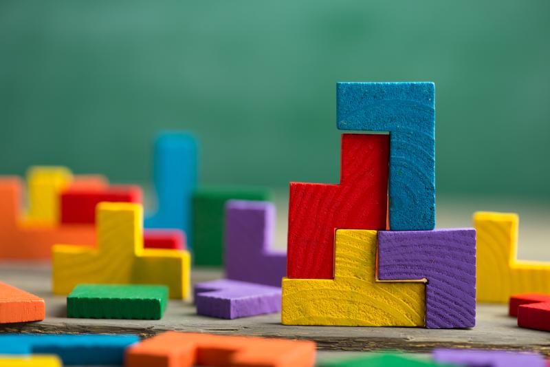 Colorful wooden Tetris-like blocks are stacked and scattered on a wooden surface with a green background.
