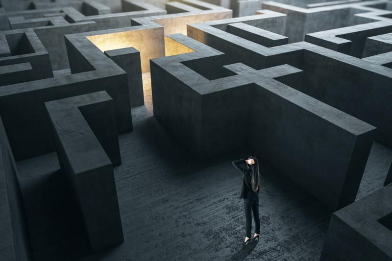 Young businesswoman in suit standing in concerete gray labyrinth.