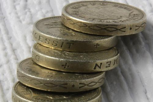 A stack of seven British one-pound coins balanced on a textured white surface.